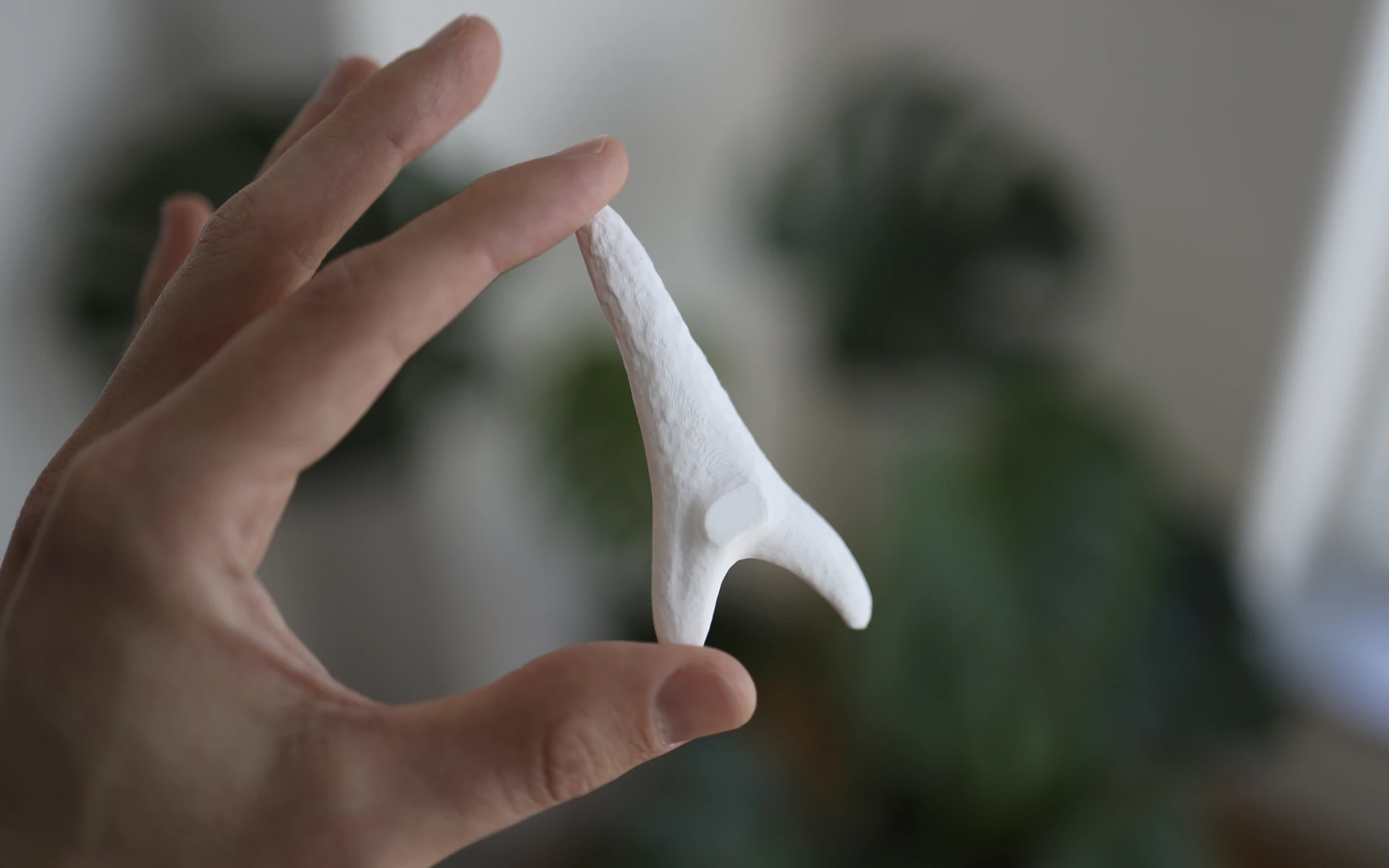 A 3D-printed shark tooth, held between the thumb and index finger.